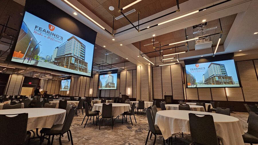 A banquet room with four large projection screens displaying the Fearing’s logo
