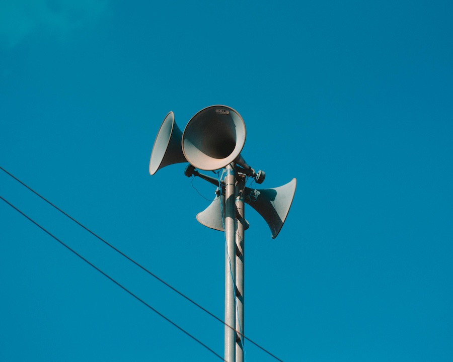 Horn speakers on a pole outdoors as part of a paging system.