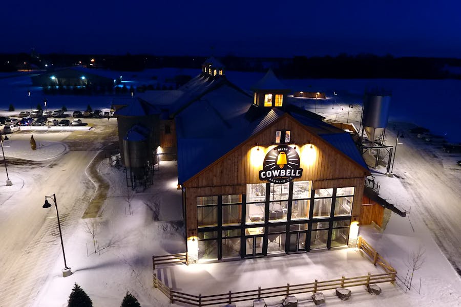 Overhead, nighttime view of a barn-like brewery called Cowbell surrounded in snow.